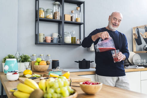 Mann gießt Smoothie in Trinkglas zu Hause - GIOF13822