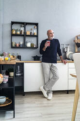 Senior man holding smoothie glass in kitchen at home - GIOF13824