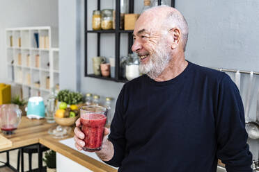 Lächelnder älterer Mann hält Smoothie-Glas in der Küche zu Hause - GIOF13826