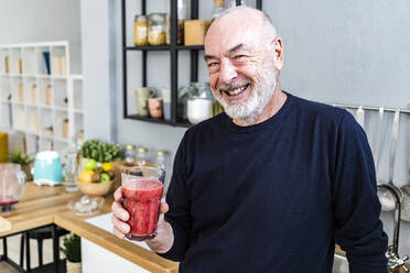 Glücklicher älterer Mann hält Smoothie-Glas zu Hause - GIOF13827