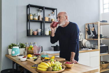 Mann trinkt Smoothie, während er an der Küchentheke steht - GIOF13828