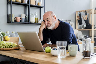 Müder Mann mit Laptop am Küchentisch - GIOF13849