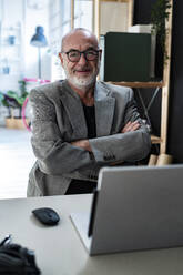 Senior businessman sitting with arms crossed sitting in studio - GIOF13860