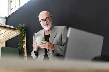 Male professional with coffee cup looking at laptop - GIOF13867