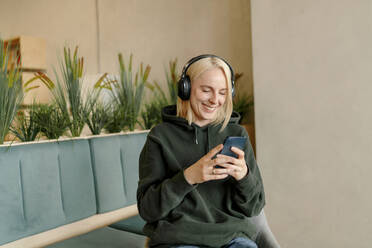 Smiling businesswoman using smart phone while listening music in office - OGF01096