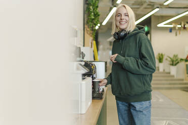 Lächelnde Geschäftsfrau bei der Kaffeezubereitung im Coworking-Büro - OGF01099