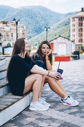 Thoughtful woman with hand on chin sitting by smiling female friend on steps - OMIF00134