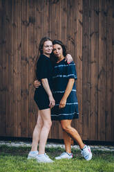 Women with arms around each other standing in front of wooden wall - OMIF00135