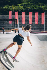 Frau auf dem Skateboard im Skatepark an einem sonnigen Tag - OMIF00140