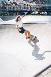 Young woman practicing skateboarding at skateboard park - OMIF00141