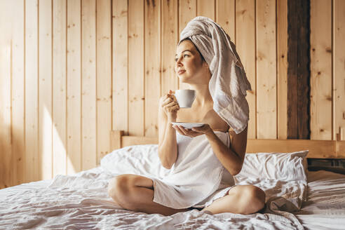 Schöne Frau schaut weg und hält eine Kaffeetasse auf dem Bett - OMIF00143