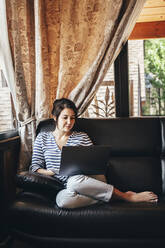 Woman using laptop while sitting on couch at home - OMIF00147