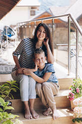 Lächelnde Mutter und Sohn sitzen auf den Stufen eines Balkons - OMIF00155