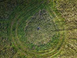 Luftaufnahme einer einsamen Frau auf einer grünen Wiese, umgeben von Reifenspuren - KNTF06497