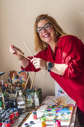 Lächelnde Frau hält Pinsel beim Malen zu Hause - DLTSF02245