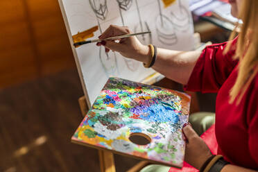 Woman painting at home while holding palette - DLTSF02248