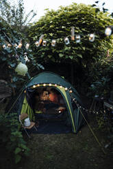 Grandmother and granddaughter camping in garden using digital tablet in tent - MOEF03954