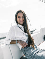 Contemplative happy female teenager sitting with crossed legs on bench of motorboat on ocean while looking at camera in Tenerife Spain - ADSF31177