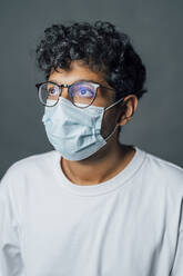 Young man wearing protective face mask against gray background - MEUF04427