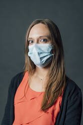 Woman with brown hair wearing protective face mask against gray background - MEUF04431