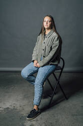 Woman sitting on chair in front of gray backdrop - MEUF04440