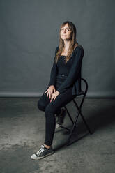 Frau sitzt auf einem Stuhl vor einem grauen Hintergrund - MEUF04445