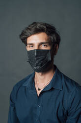 Man wearing black face mask against gray background - MEUF04454