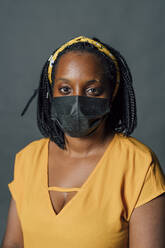 Junge Frau mit geflochtenem Haar und Gesichtsschutzmaske vor grauem Hintergrund - MEUF04460
