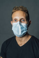 Man with blond hair wearing protective face mask against gray background - MEUF04473