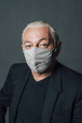 Älterer Mann mit Gesichtsschutzmaske vor grauem Hintergrund - MEUF04485