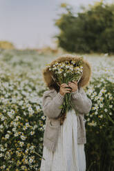 Mädchen bedeckt Gesicht mit Blumenstrauß auf Feld - SSGF00017