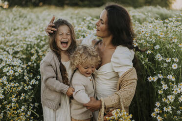 Mutter mit fröhlicher Tochter und Sohn inmitten von blühenden Pflanzen auf einem Feld - SSGF00020