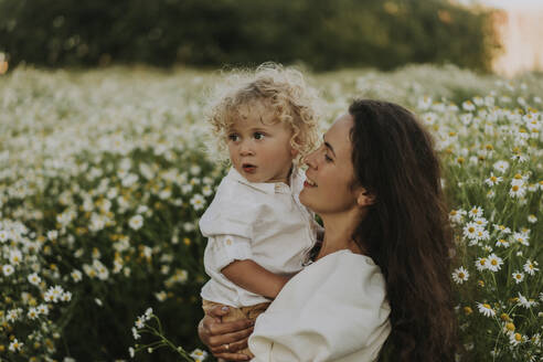 Smiling woman carrying blond baby boy at field - SSGF00029