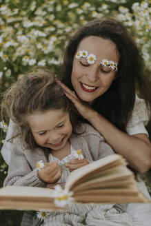 Fröhliche Mutter und Tochter mit Blumen und Buch auf einem landwirtschaftlichen Feld - SSGF00042