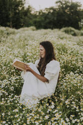 Frau liest ein Buch, während sie auf einem Blumenfeld sitzt - SSGF00043