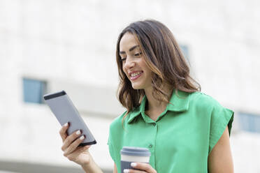 Smiling woman with disposable cup using digital tablet - EIF02180