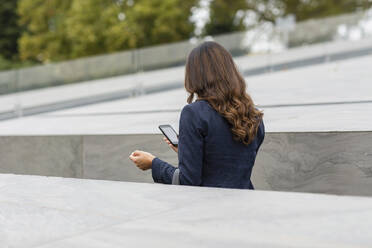 Geschäftsfrau benutzt Mobiltelefon inmitten einer Stützmauer - EIF02183