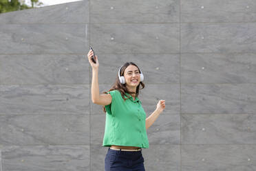 Happy woman dancing in front of gray wall - EIF02187