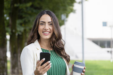 Happy young woman holding mobile phone and disposable coffee cup - EIF02192