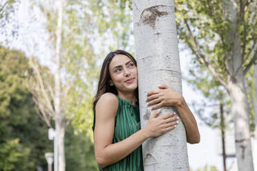 Smiling young woman hugging tree at park - EIF02200