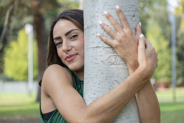 Beautiful young woman hugging tree in park - EIF02201