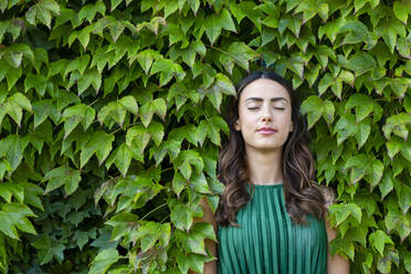 Beautiful young woman with eyes closed leaning on ivy leaves - EIF02204