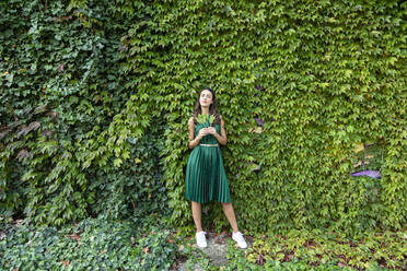 Junge Frau hält Blätter vor grünen Efeupflanzen - EIF02207