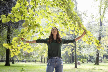 Smiling woman holding branches at park - EIF02225