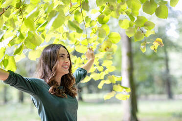 Happy woman holding branches at park - EIF02228