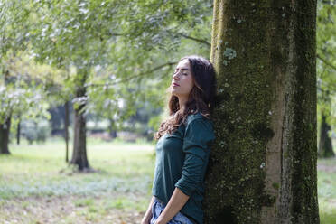 Beautiful woman with eyes closed leaning on tree trunk - EIF02230