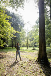 Young woman walking toward tree at park - EIF02233