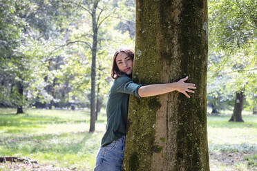Beautiful young woman hugging tree in park - EIF02235