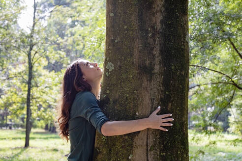 Frau, die sich umarmt und einen Baum im Park betrachtet - EIF02236