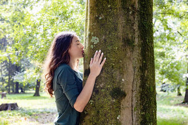 Young woman kissing tree trunk at park - EIF02237